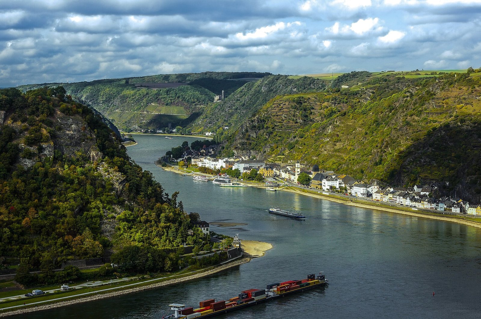 Der Rhein an der Loreley: der Strom windet sich zwischen bewaldeten Schieferhängen, auf dem Wasser ein Frachtschiff.
